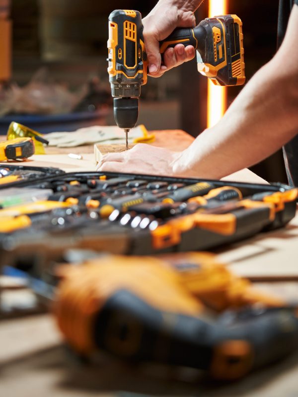 different tools are on the workbench. focus on the hands of a worker who drills with a drill driver with a replaceable battery. High quality photo